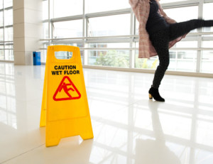 Person slipping on a wet floor next to a Caution Wet floor sign