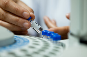 Laborant inserting laboratory glass bottle in a chromatograph vial